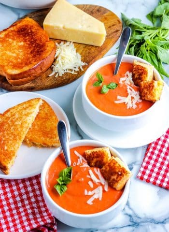 Two bowls of homemade tomato soup with grilled cheese sandwiches.