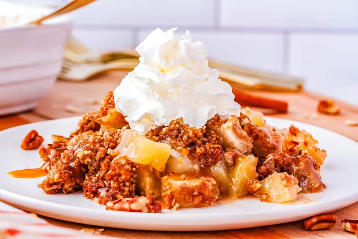 A scoop of apple crisp on a plate and topped with whipped cream.