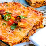 The chicken enchilada casserole inside the baking dish with a few slices taken out of it.