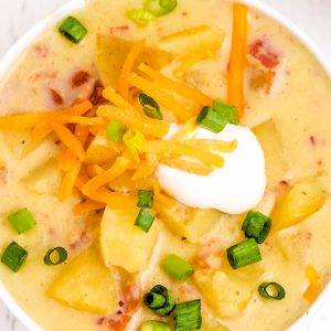 A close up picture of creamy potato soup in a white bowl.