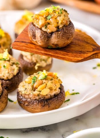 A spoon ;siting up one of the goat cheese Stuffed Mushrooms from a serving platter.