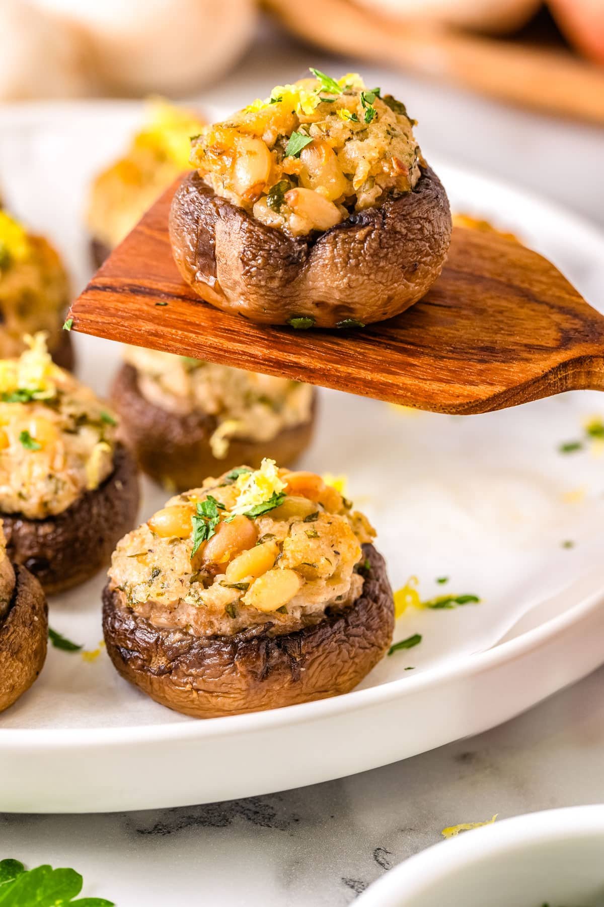 A spoon ;siting up one of the goat cheese Stuffed Mushrooms from a serving platter.