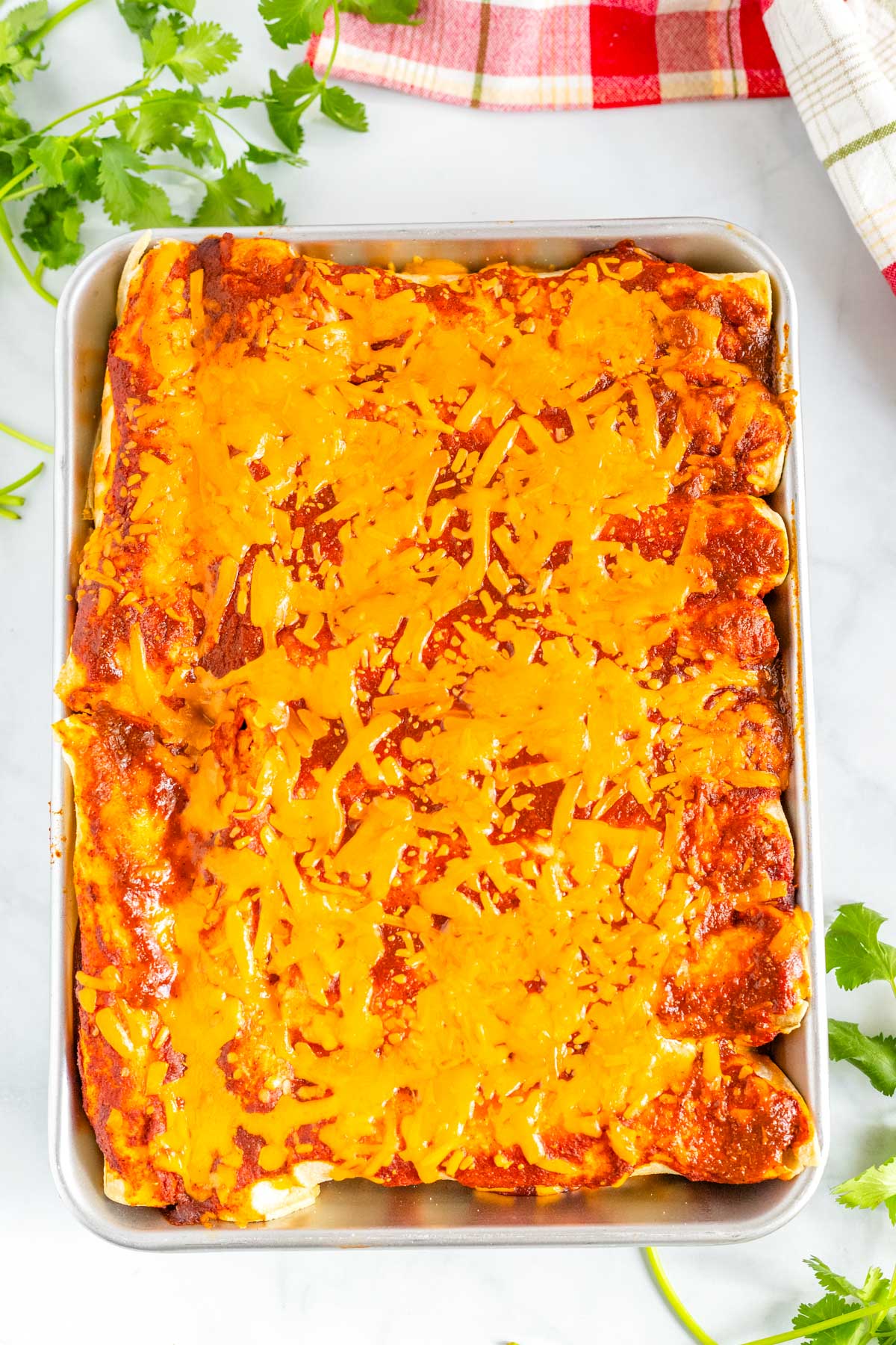 A pan of Shredded Beef Enchiladas smothered in red enchilada sauce and shredded cheese.