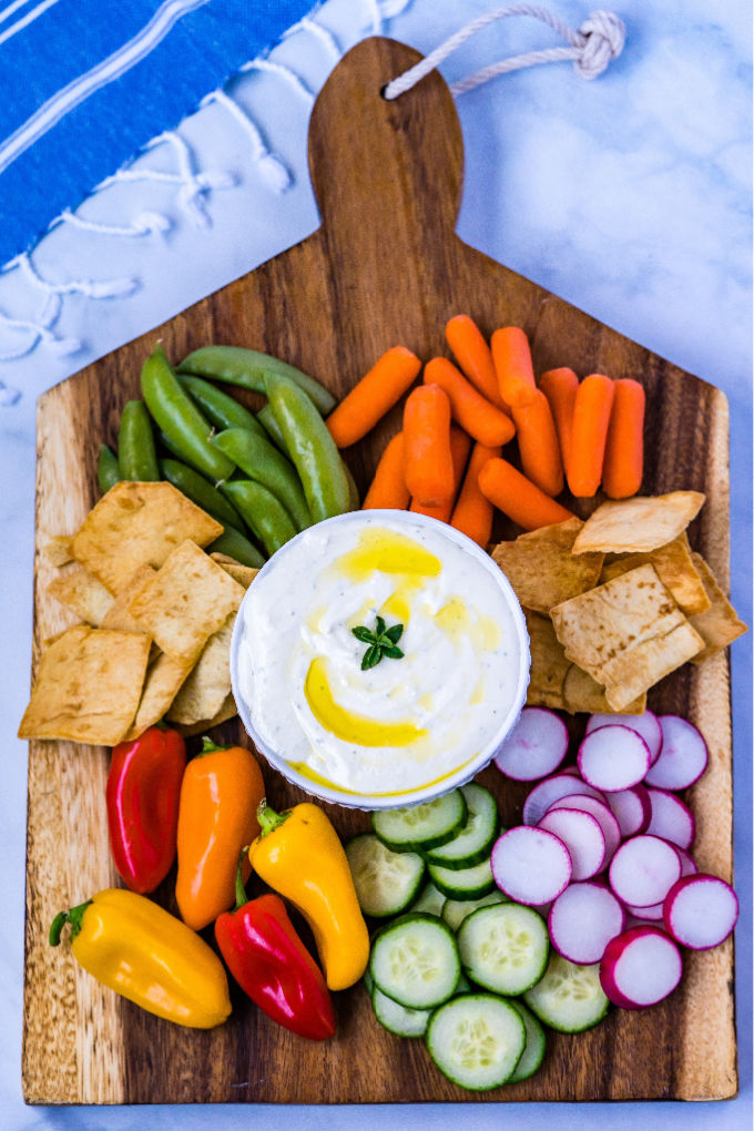 An overhead picture of whipped feta dip in a white bowl surrounded by veggies and pita chips for dipping. 