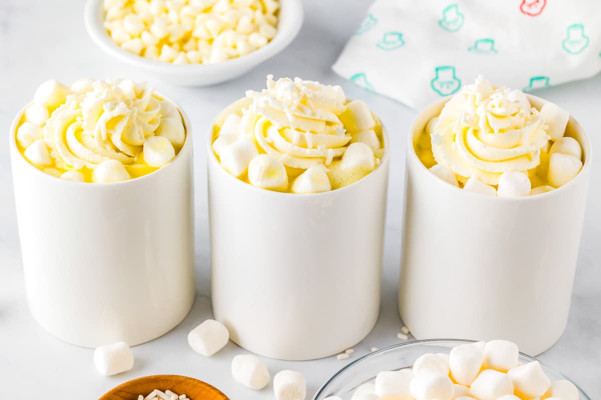 Three mugs of white chocolate hot cocoa in a row on a countertop.