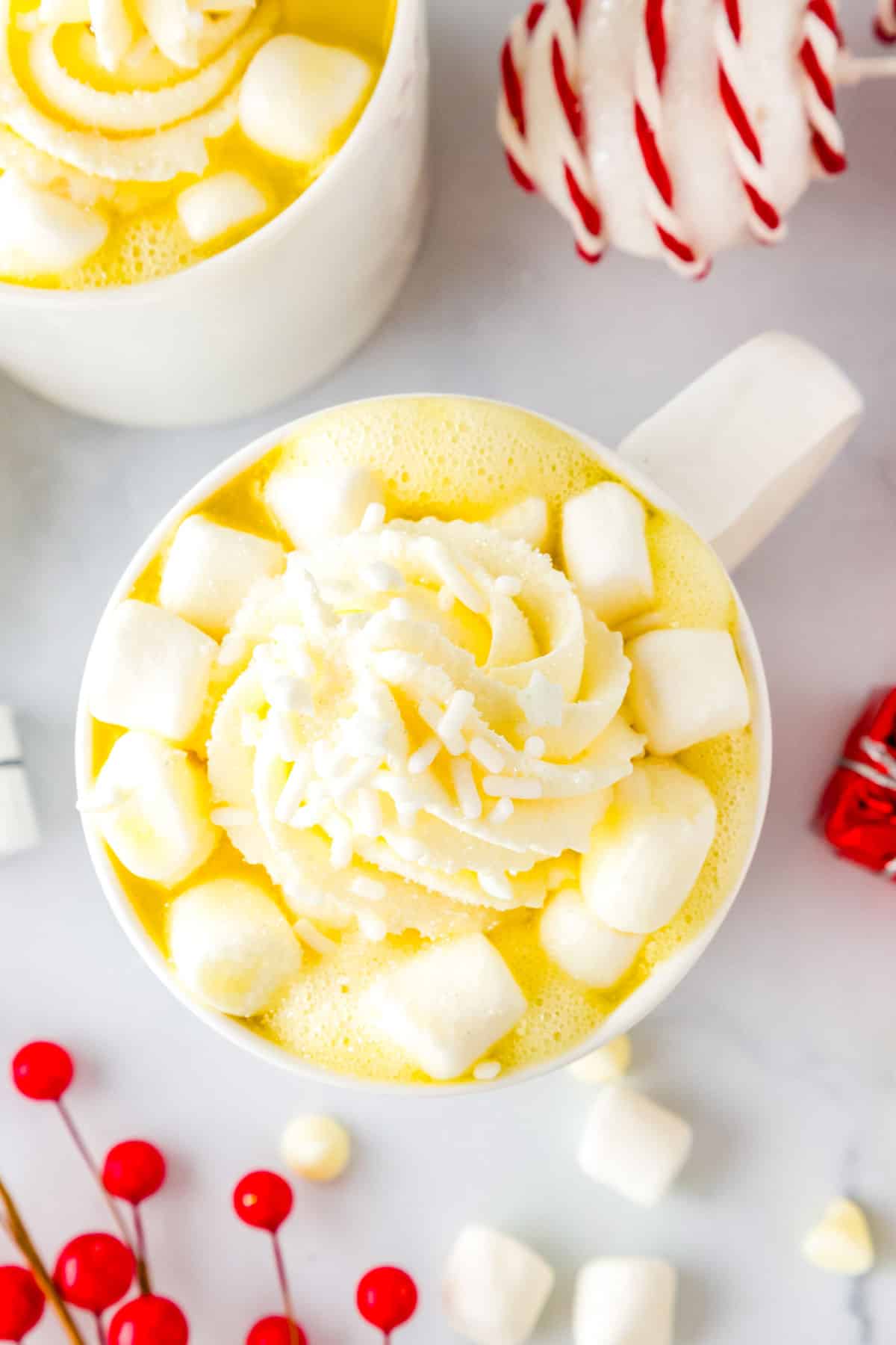 A cup of white hot chocolate garnished with whipped cream, mini marshmallows, and sprinkles.