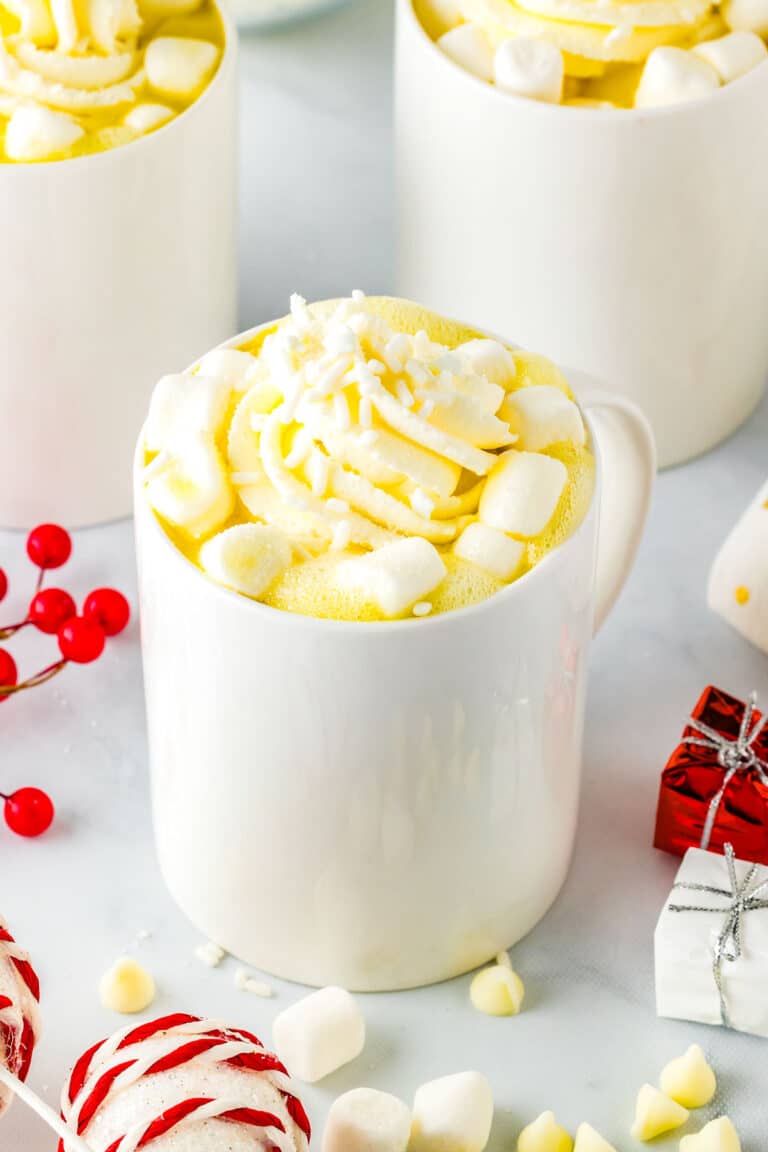 A mug of white hot chocolate surrounded by mini marshmallows and small Christmas decorations.