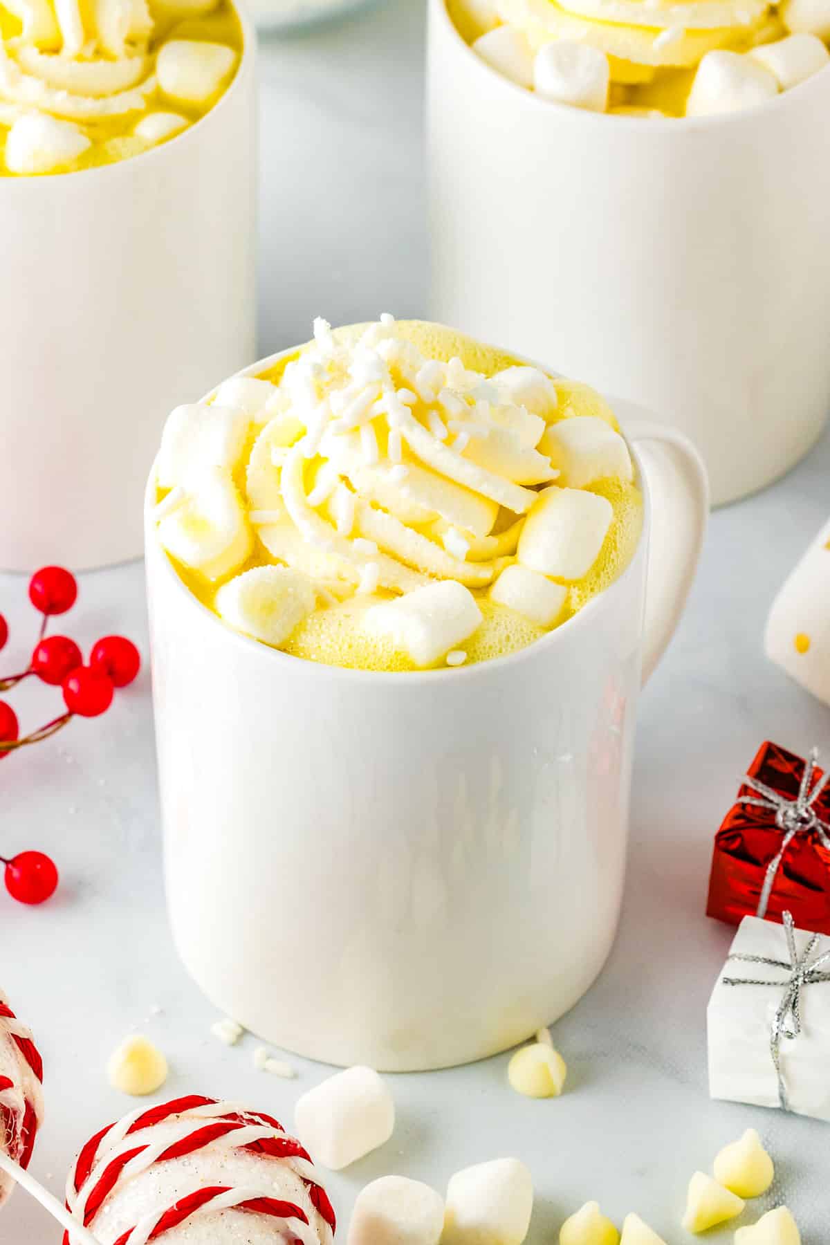 A mug of white hot chocolate surrounded by mini marshmallows and small Christmas decorations.