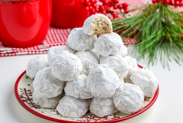 A plate full of pecan snowball cookies stacked on top of each other.