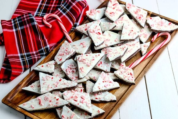 Peppermint bark on a serving tray with a plaid towel and candy canes in the background.