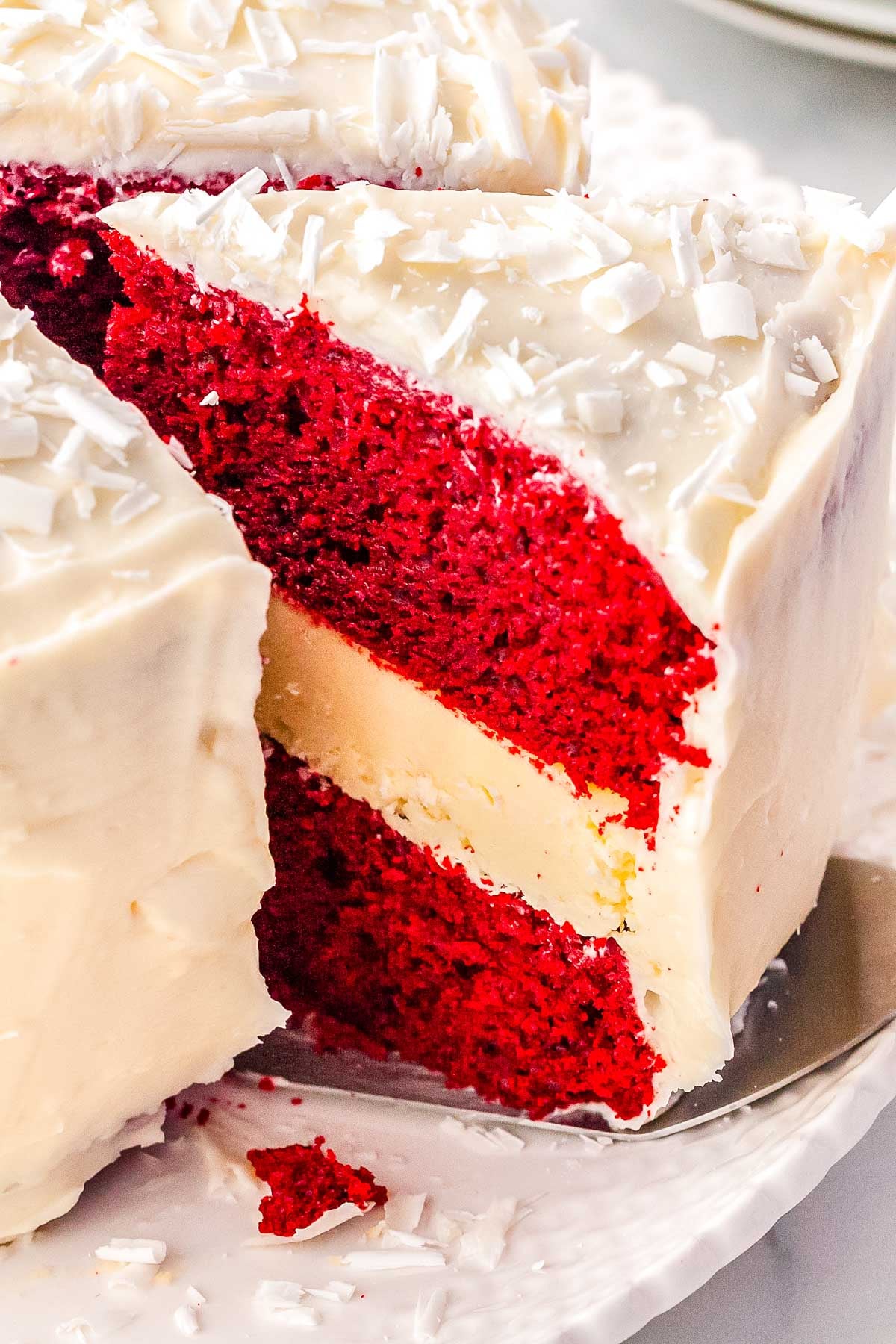 A slice being pulled from the cake, revealing the thick, creamy cheesecake layer sandwiched between two moist red velvet cake layers.