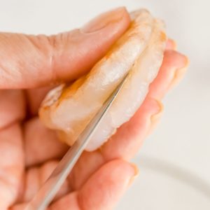 A knife slicing into the back of a shrimp that has been peeled.