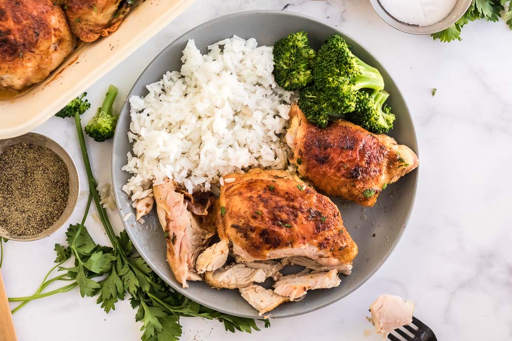 The finished oven baked chicken on a grey plate with rice and broccoli. 