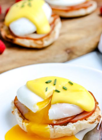 Eggs Benedict on a white plate with the yolk running out.