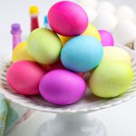 How to Dye Easter Eggs with Food Coloring. The finished eggs are on a white cake pedestal.