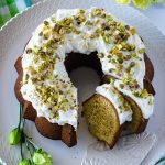 An overhead picture of Pistachio Bundt Cake that is made from scratch. Lemons and green and yellow flowers surround the cake.