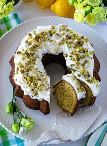 An overhead picture of Pistachio Bundt Cake that is made from scratch. Lemons and green and yellow flowers surround the cake.