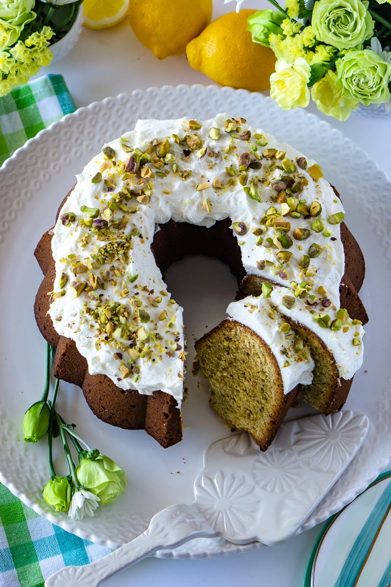 An overhead picture of Pistachio Bundt Cake that is made from scratch. Lemons and green and yellow flowers surround the cake. 