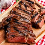 A close up picture of grilled strip steak cut into slices on a cutting board.