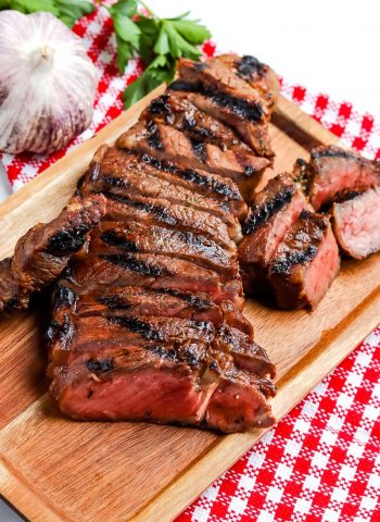 Grilled New York Strip Steak sliced on a wooden cutting board.