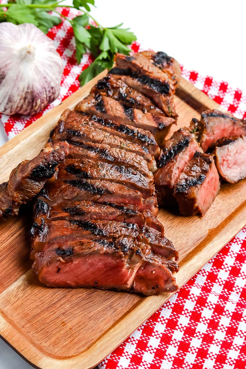 Grilled New York Strip Steak sliced on a wooden cutting board.