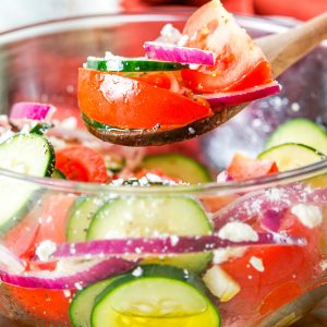 A close up picture of Cucumber Tomato Feta Salad in a clear glass serving bowl.