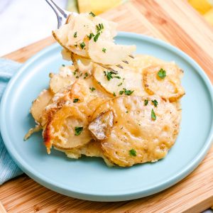 A close up picture of crockpot cheesy scalloped potatoes on a plate and a fork.