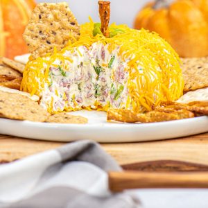 The finished Pumpkin Cheese Ball on a white serving platter surrounded by crackers and pretzels.