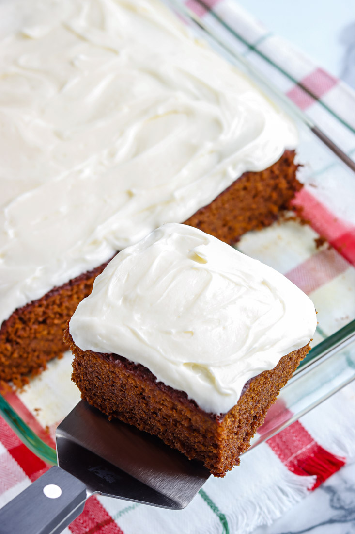 A spatula taking a piece of Gingerbread Cake With Cream Cheese Frosting out of the sheet cake.