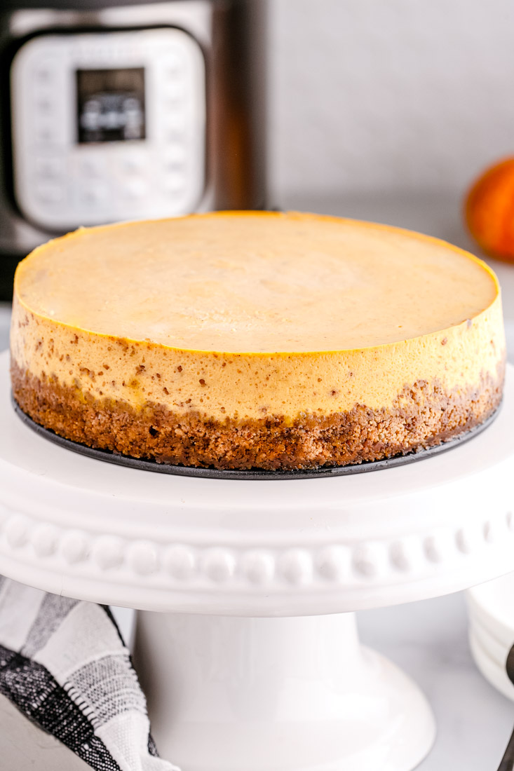 The finished Instant Pot Pumpkin Cheesecake on a white cake stand.