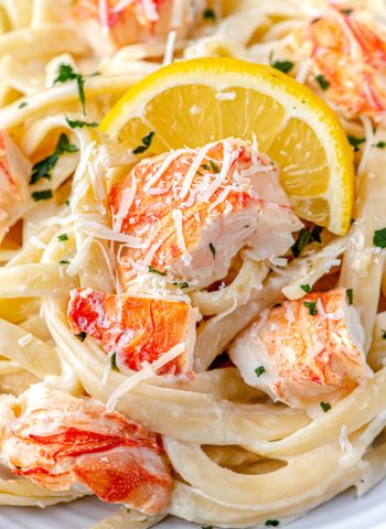 A close up picture of the finished Lobster Alfredo recipe on a white plate with a lemon slice.