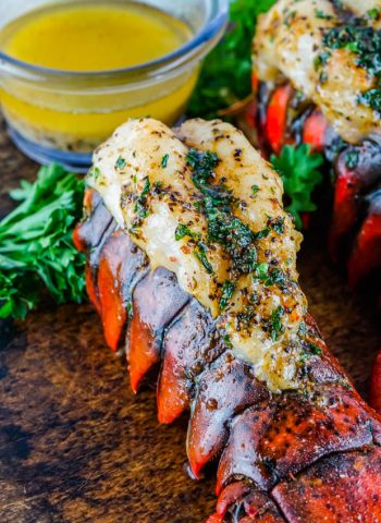 The finished Smoked Lobster Tail on a wooden cutting board with a dish of melted butter in the background.
