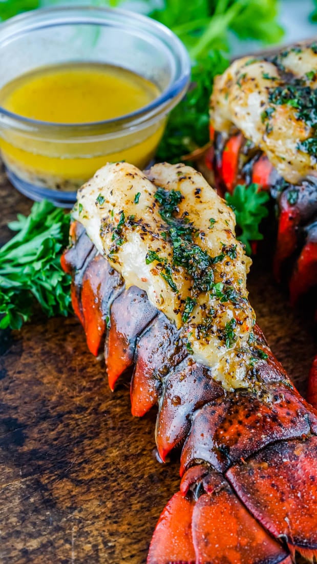 The finished Smoked Lobster Tail on a wooden cutting board with a dish of melted butter in the background. 