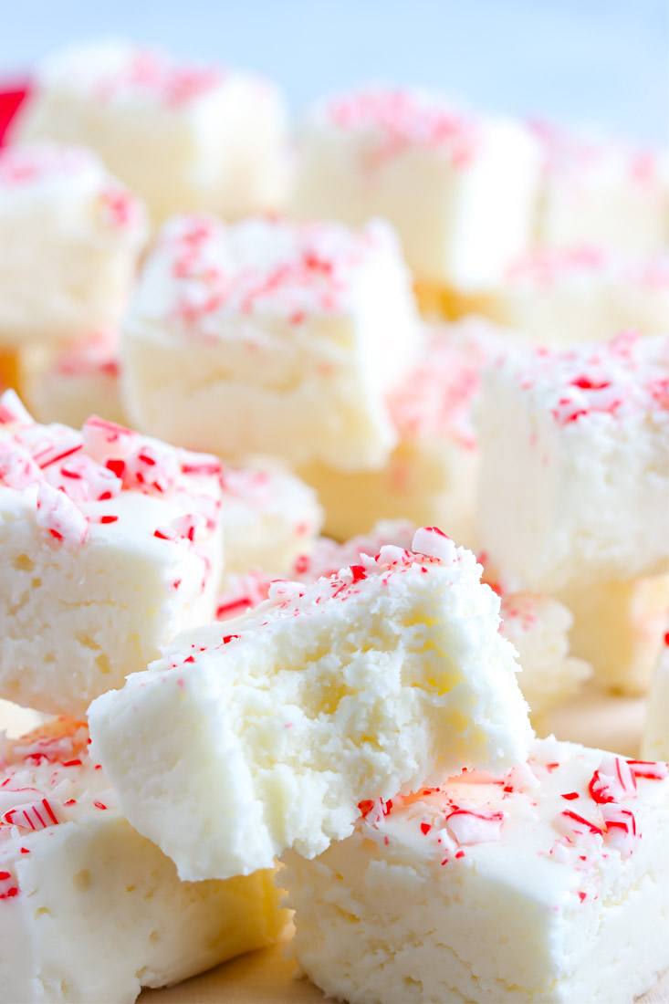 A close up picture of squares of White Chocolate Peppermint Fudge, one with a bite taken out of it.