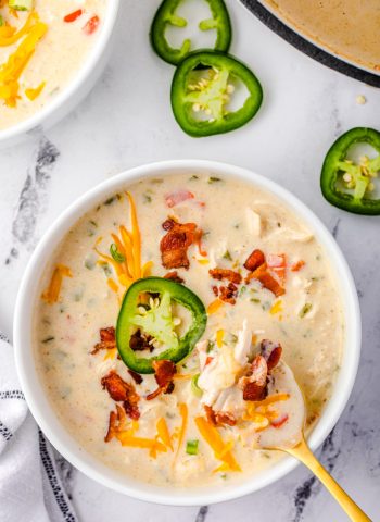 An overhead picture of the finished Jalapeno Popper Soup on a white bowl. The soup is garnished with sliced jalapeños, bacon, and cheese.