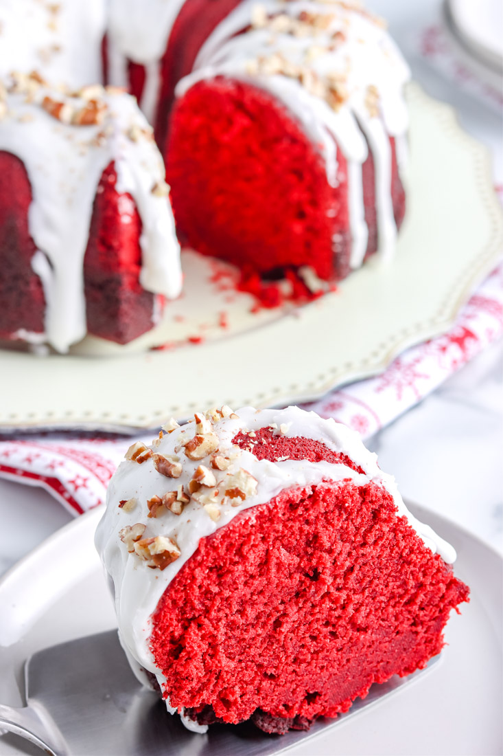 A slice of Red Velvet Bundt Cake on a white plate with a drizzle of cream cheese glaze.