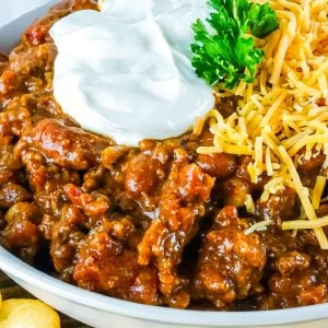 A close up picture of the finished Smoked Chili in a white bowl topped with cheese and sour cream.