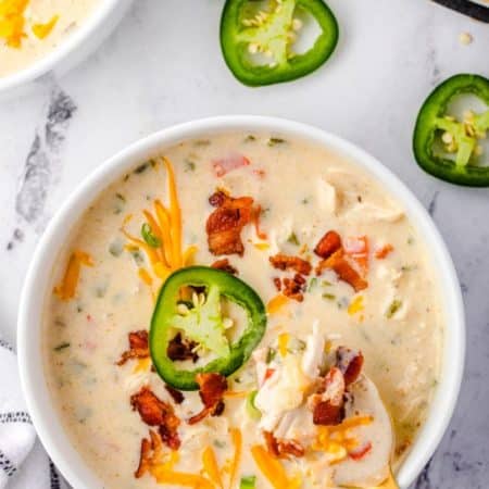 An overhead picture of the finished Jalapeno Popper Soup on a white bowl. The soup is garnished with sliced jalapeños, bacon, and cheese.