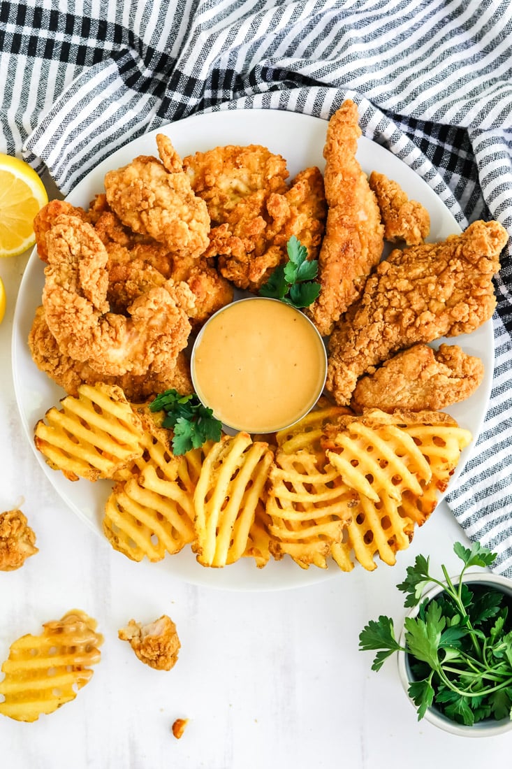 An overhead picture of a platter of waffle fries, chicken fingers, and this home Ade Chick Fil A Sauce recipe.