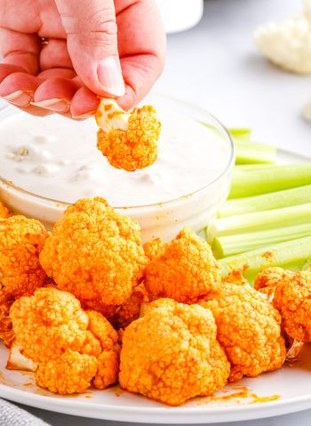 A hand dipping Buffalo Cauliflower Biters into blue cheese dressing.