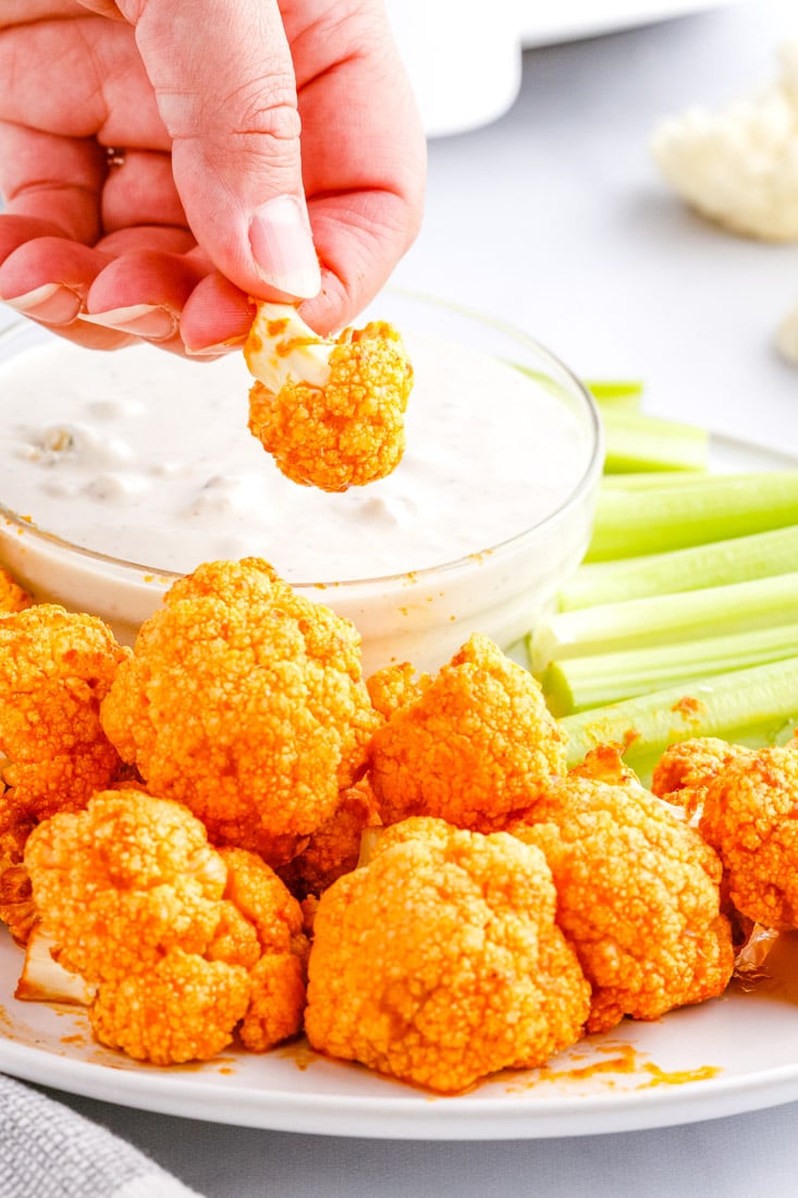 A hand dipping Buffalo Cauliflower Biters into blue cheese dressing.
