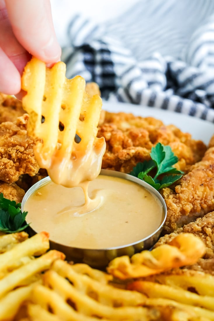 a platter of waffle fries and chicken fingers with Chick Fil A Sauce.