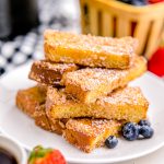 A pile of Air Fryer French Toast Sticks on a white plate. The French Toast sticks have been dusted with powdered sugar.