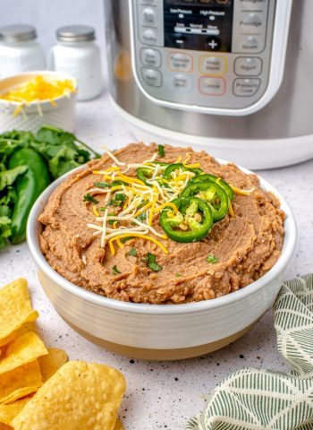 The finished Instant Pot Refried Beans in a serving bowl garnished with shredded cheese, jalapeños, and cilantro.