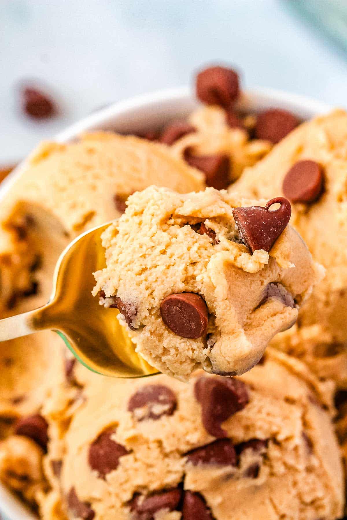 A spoon picking up some cookie dough from a mound of cookie dough.
