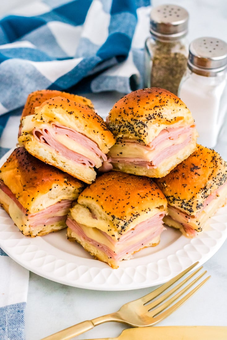 hot ham and cheese sliders stacked on each other on a white plate.