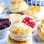 Old Fashioned Buttermilk Biscuits stacked on top of each other and some have jam on them.