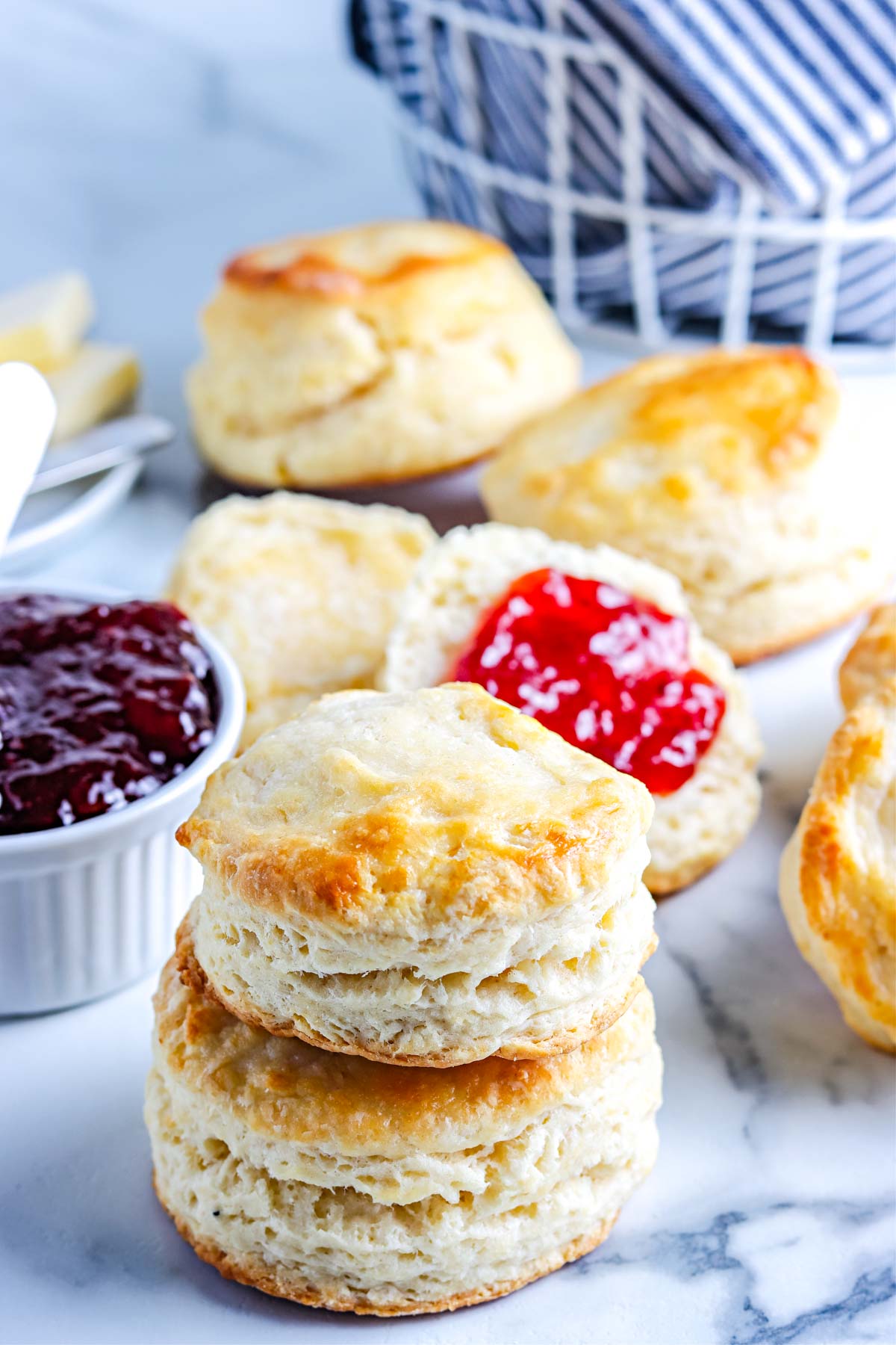 Old Fashioned Buttermilk Biscuits stacked on top of each other and some have jam on them. 
