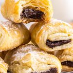 A stack of Puff Pastry Chocolate Croissants, one with a bite taken out of it.