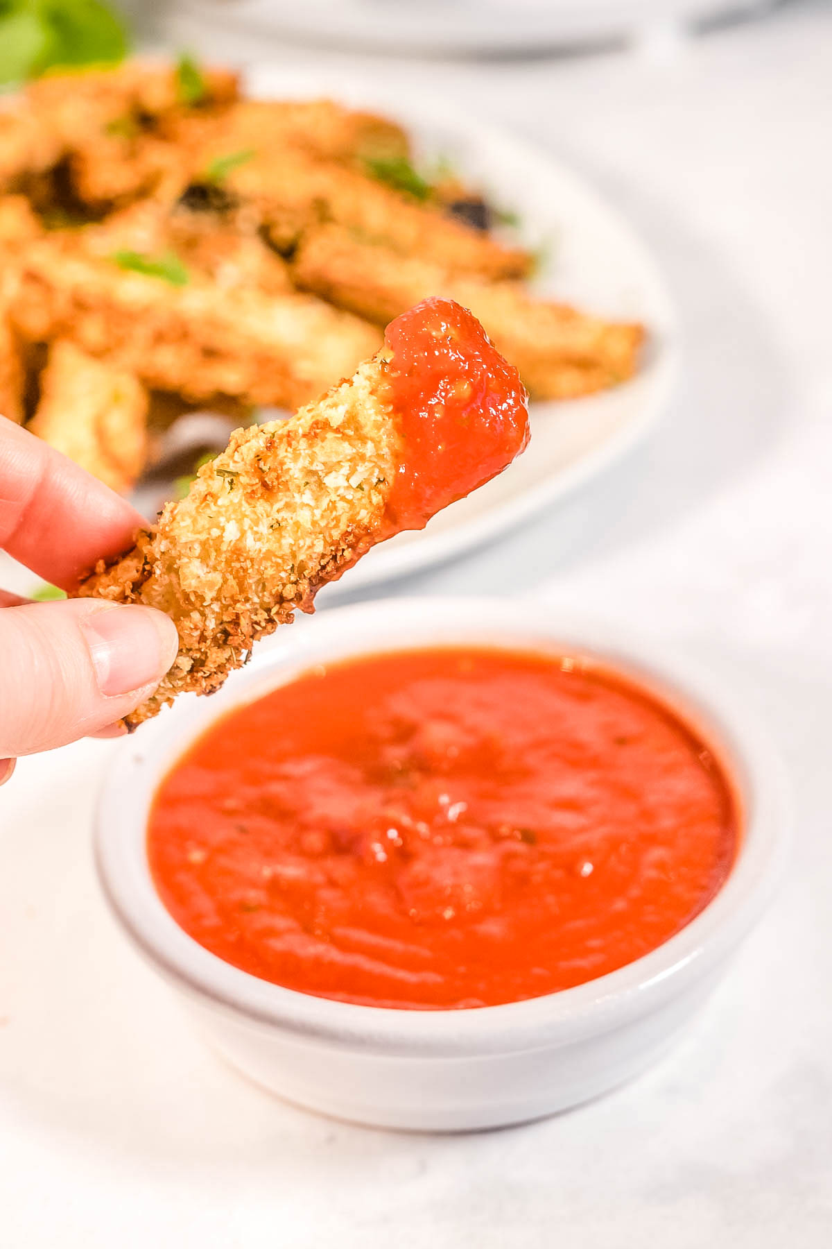 A eggplant fry being dipped into marinara sauce.